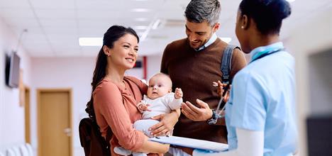 A couple holds a baby while interacting with a healthcare professional in a hospital setting.