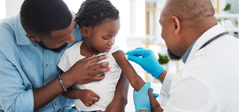 A child receives a vaccination while being comforted by a parent, with a healthcare professional administering the shot.